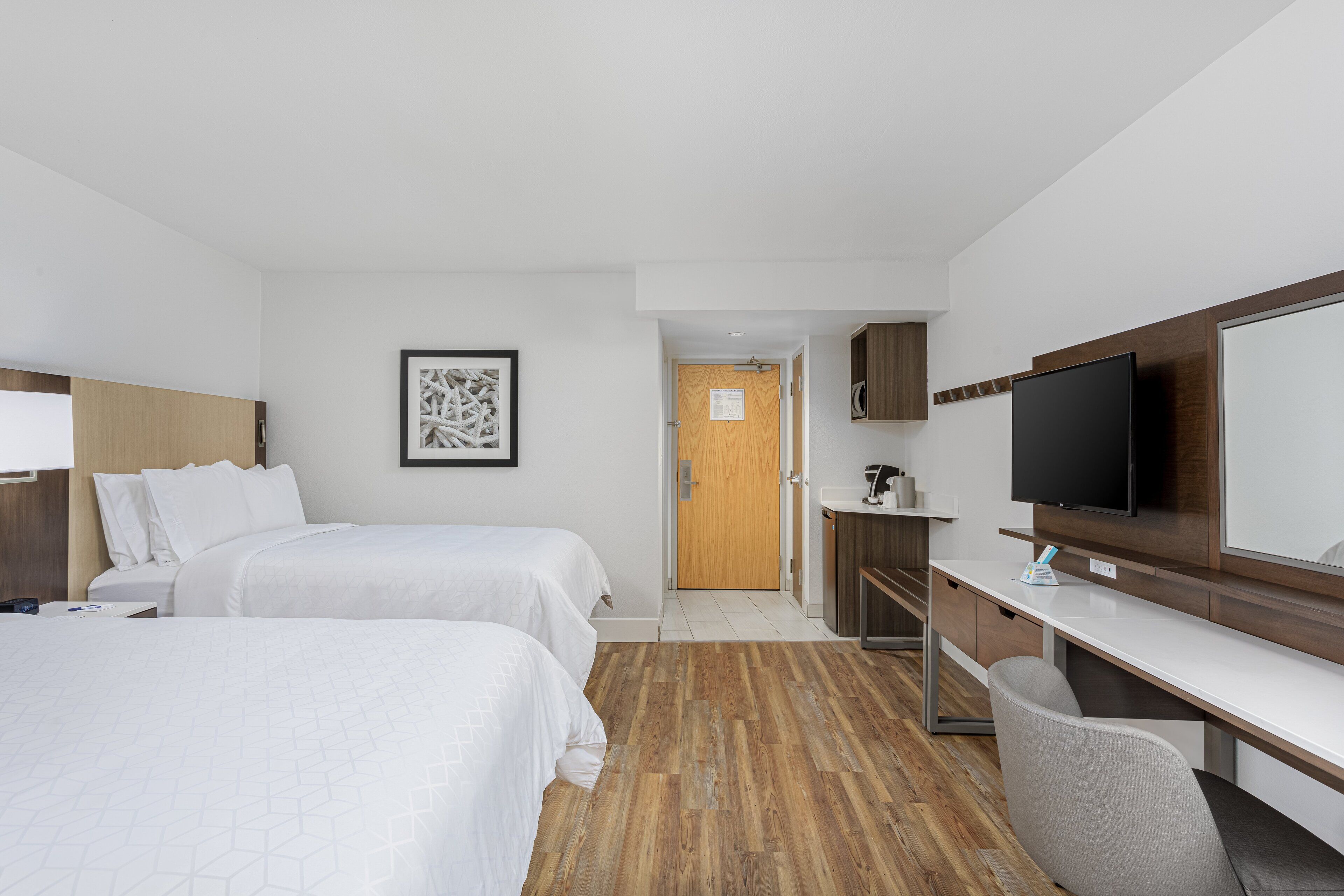 A hotel room with two beds, a desk, a chair, a television, and a bathroom visible through an open door.