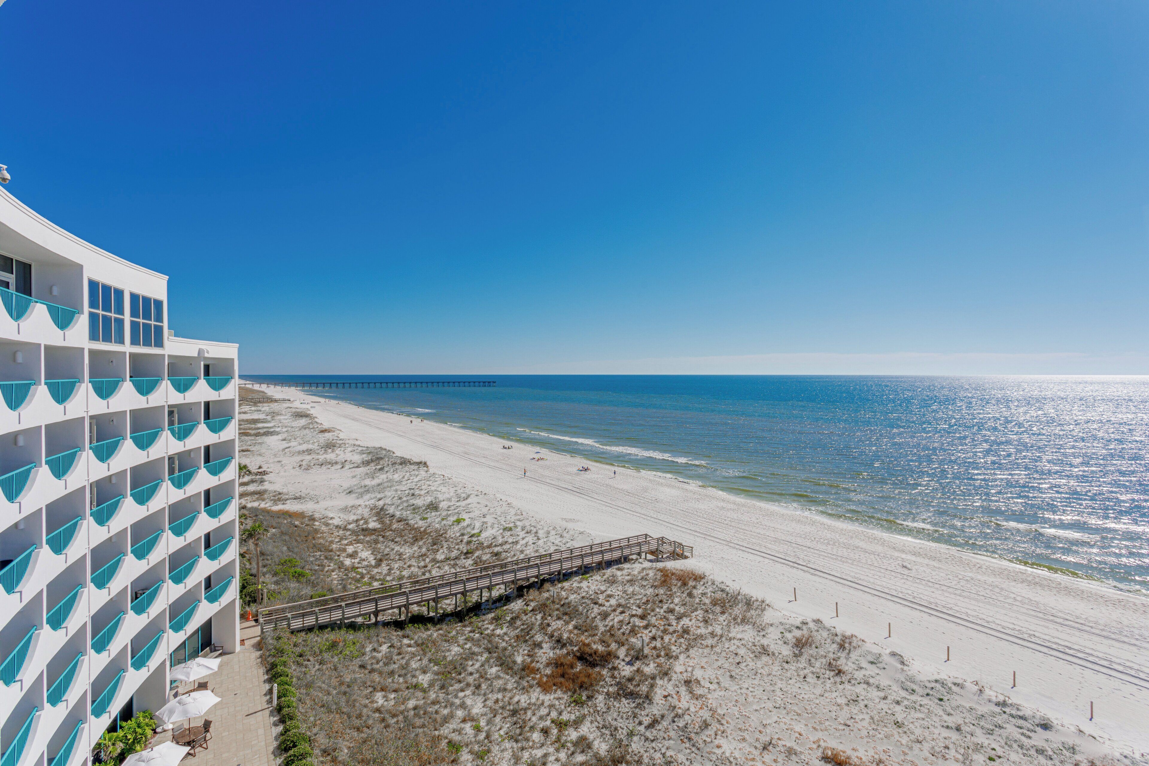 Ein Strandhotel mit einer langen Pier, die sich ins Meer erstreckt, einem Sandstrand und einem strahlend blauen Himmel.