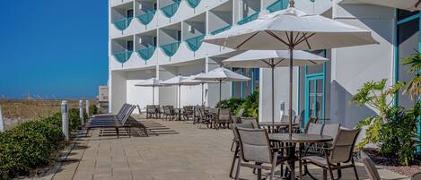 A hotel patio with outdoor seating, umbrellas, and a view of the ocean.