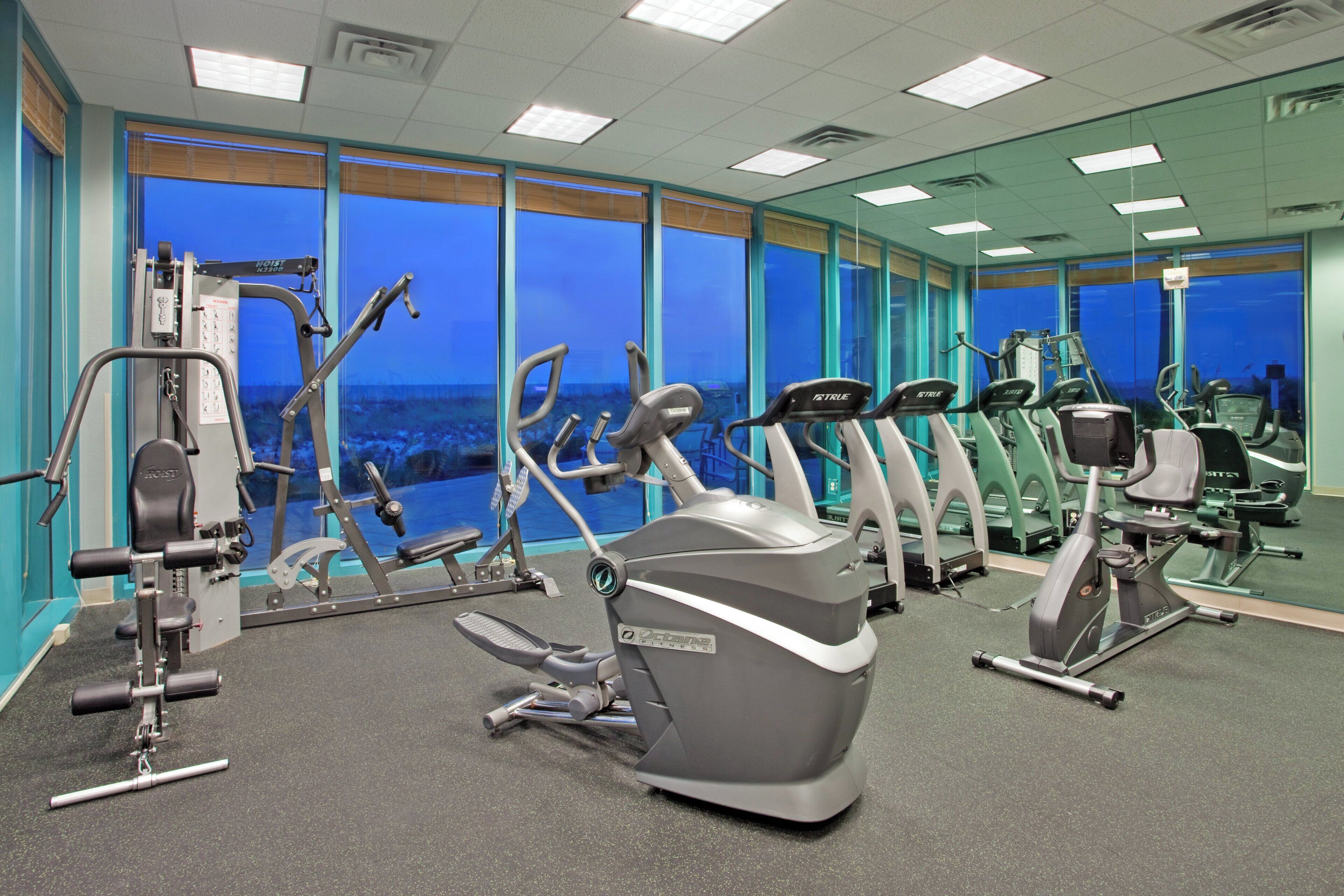 A gym with various exercise equipment, large windows, and a view of the cityscape.
