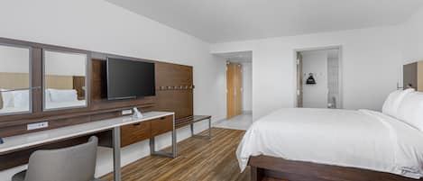 A modern hotel room with a wooden floor, a large bed, a desk with a chair, a flat-screen TV, and a wardrobe.