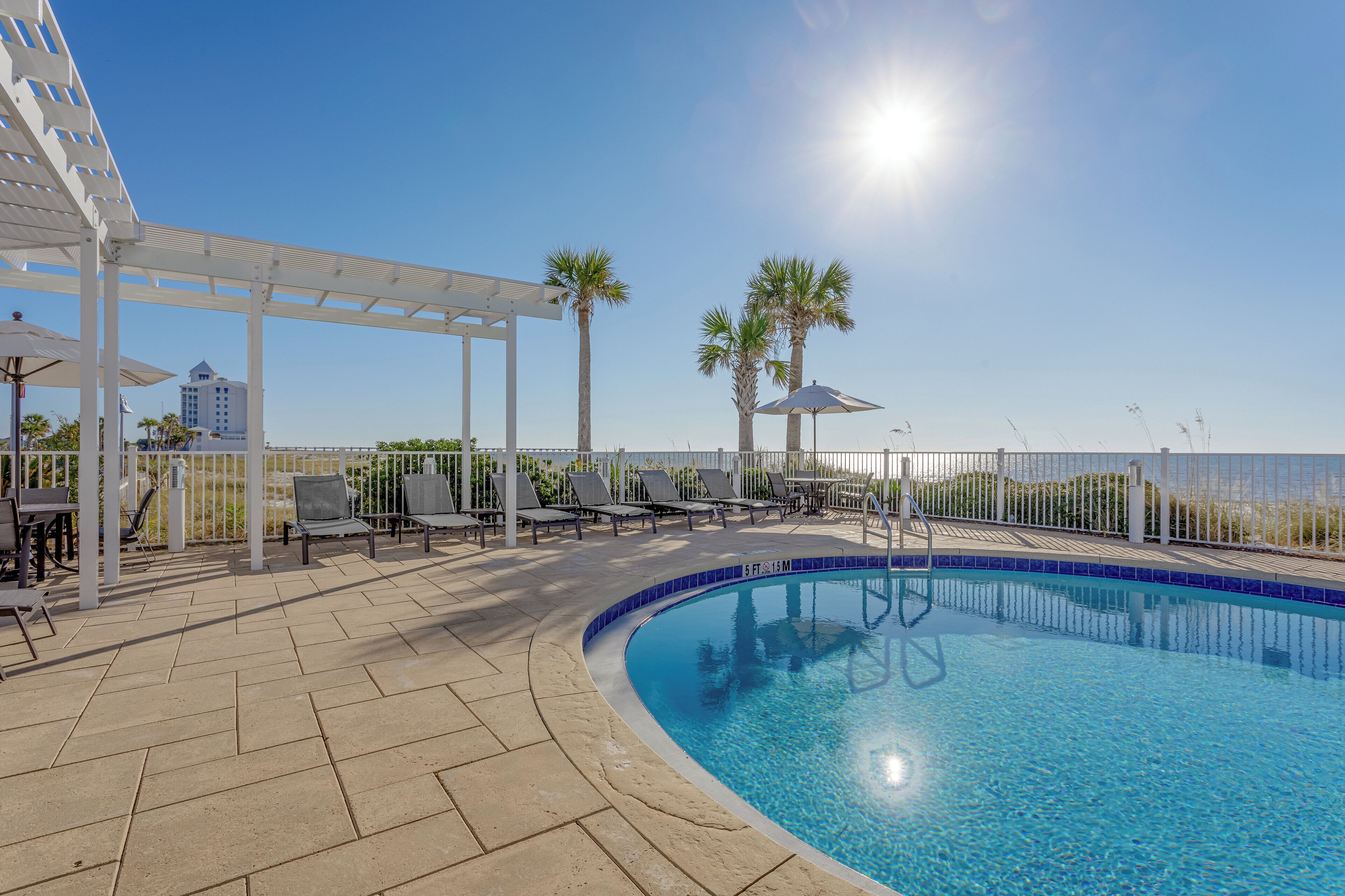 A pool area with lounge chairs, umbrellas, and a pergola.