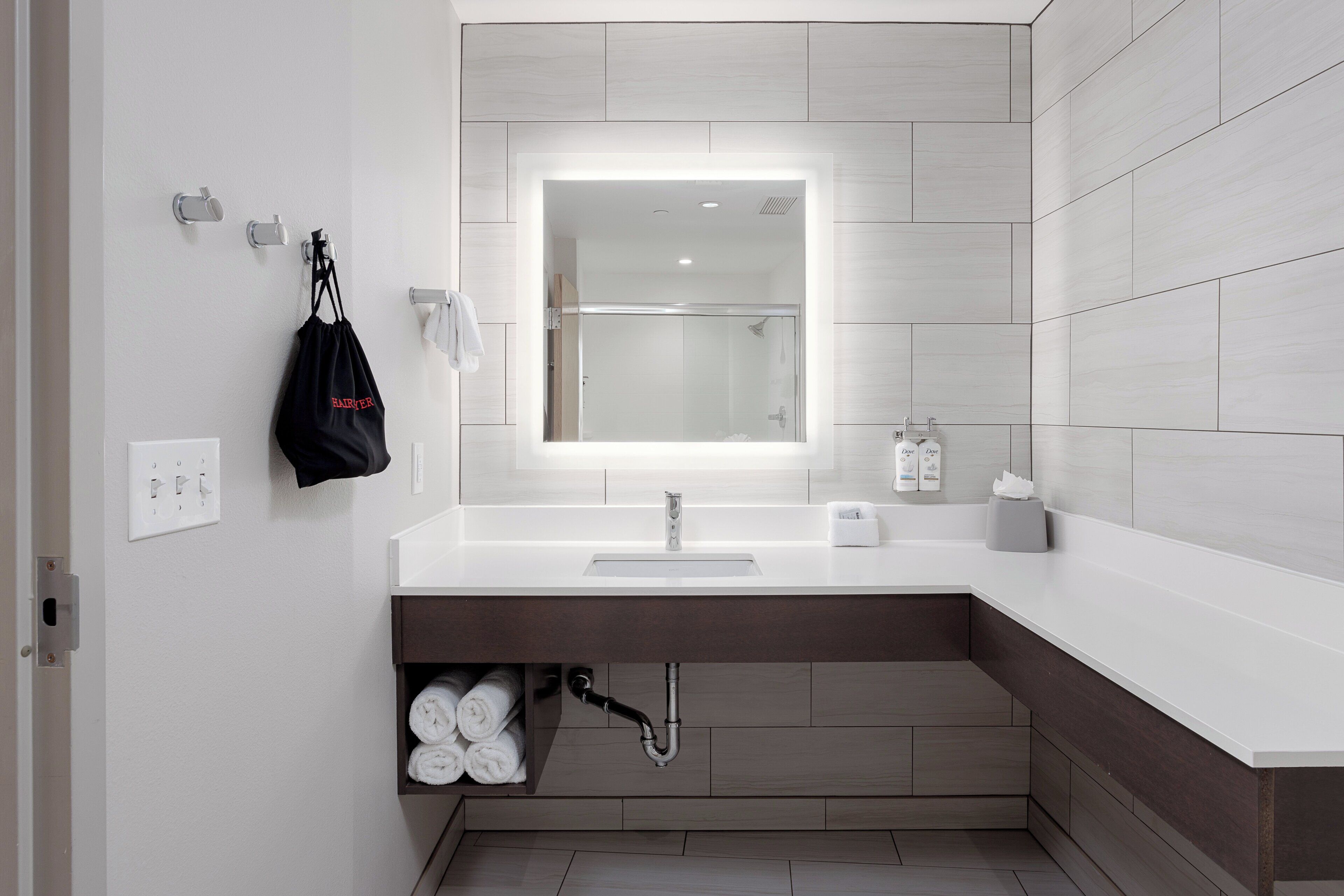 A modern bathroom with a large mirror, white sink, and a towel rack.