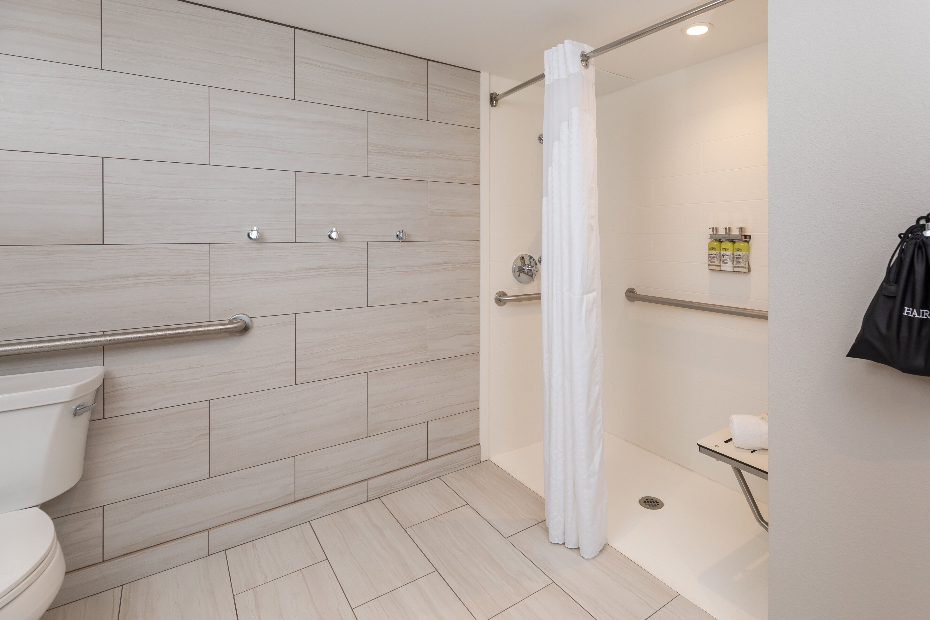 Ein modernes Badezimmer mit Dusche, Toilette und Haltegriffen.