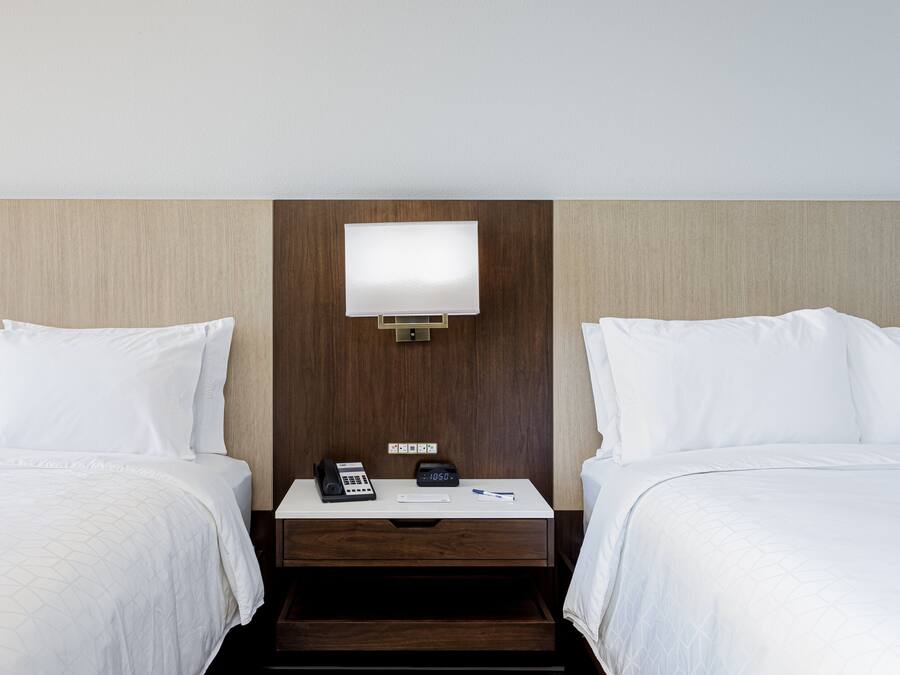 Et hotelværelse med to senge, et natbord med telefon og vækkeur, samt en lampe monteret på væggen.