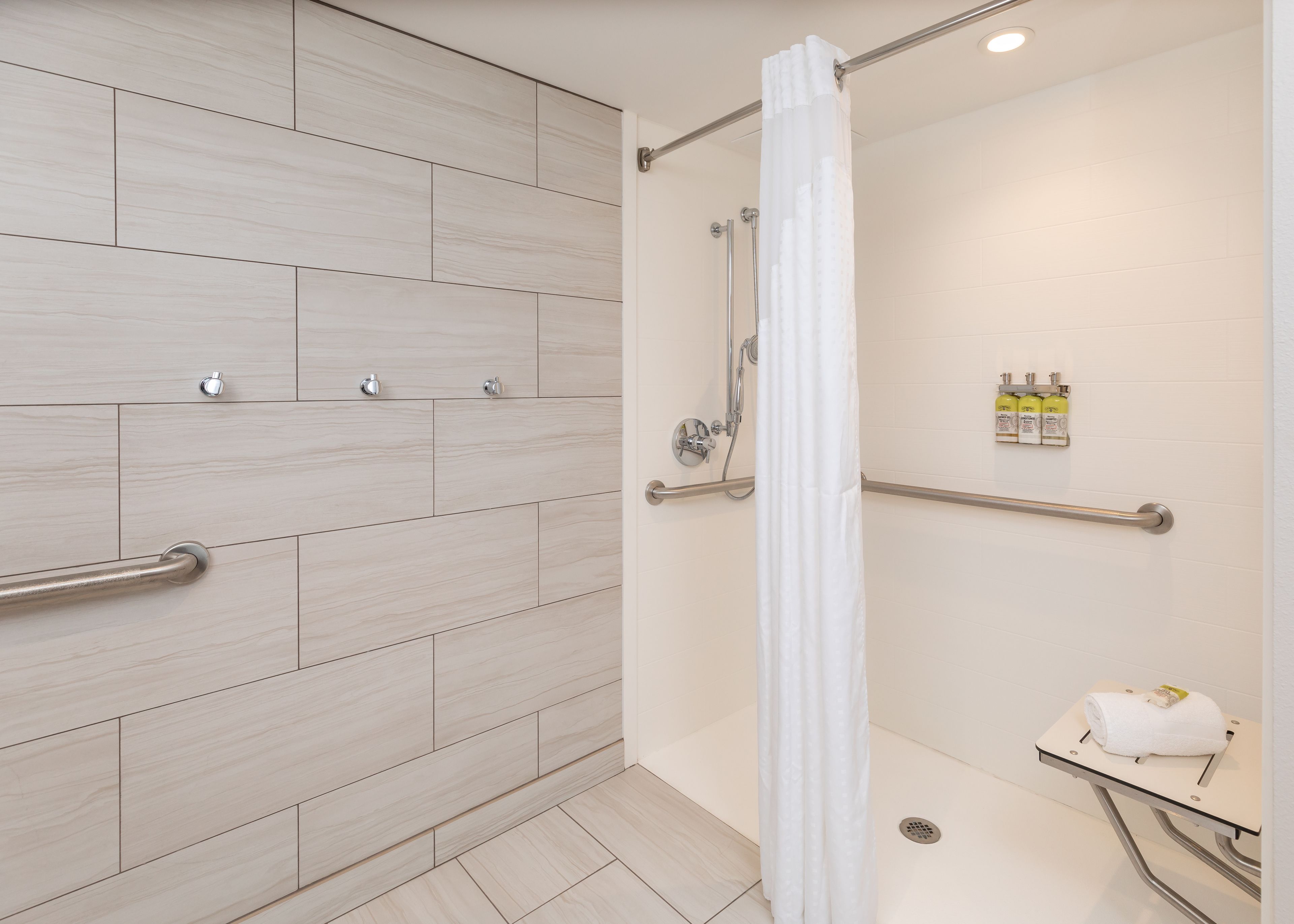 A modern bathroom with a shower, grab bars, and a towel rack.