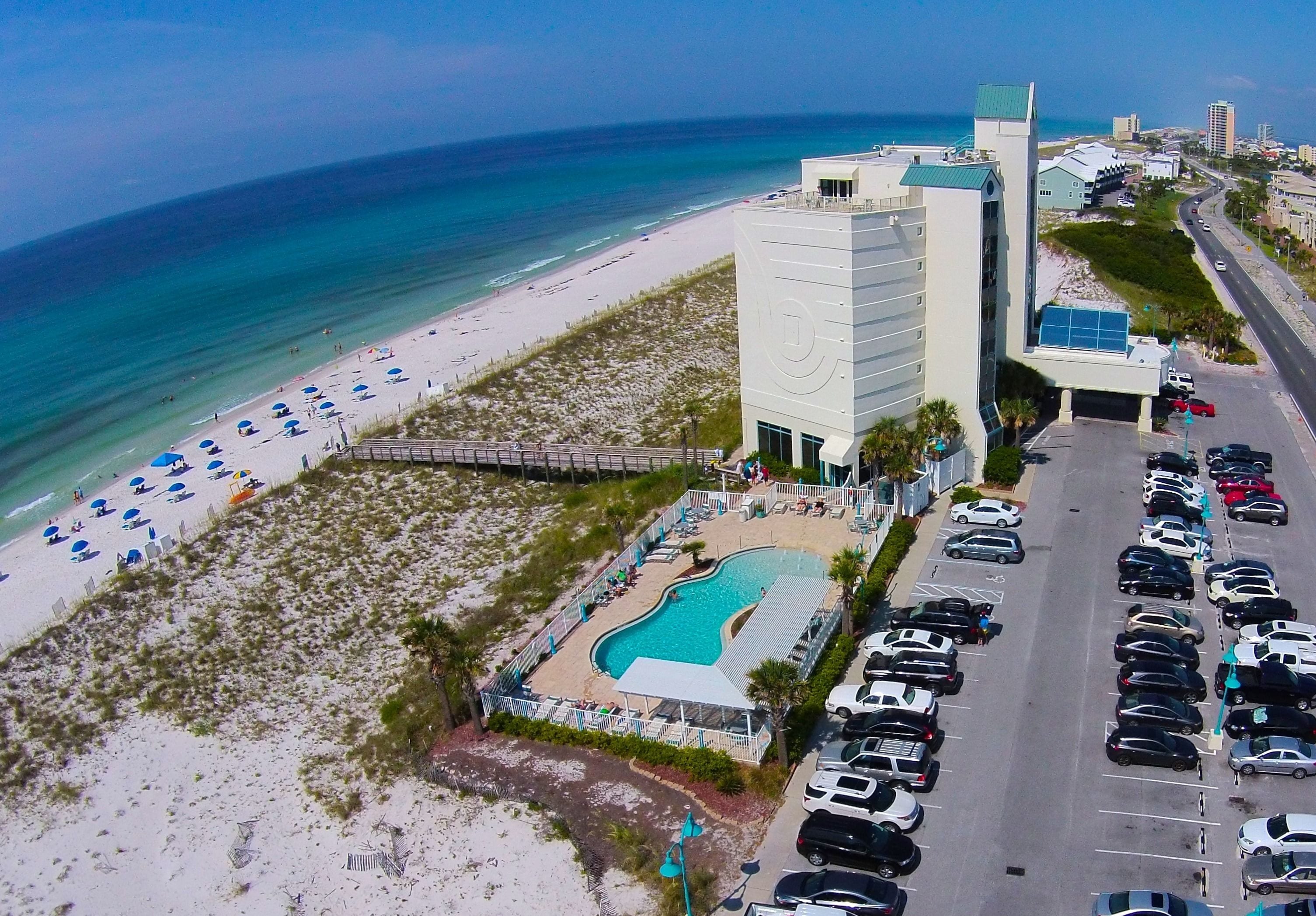 Ein Hotel aus der Vogelperspektive mit Pool, Strand und Parkplatz.