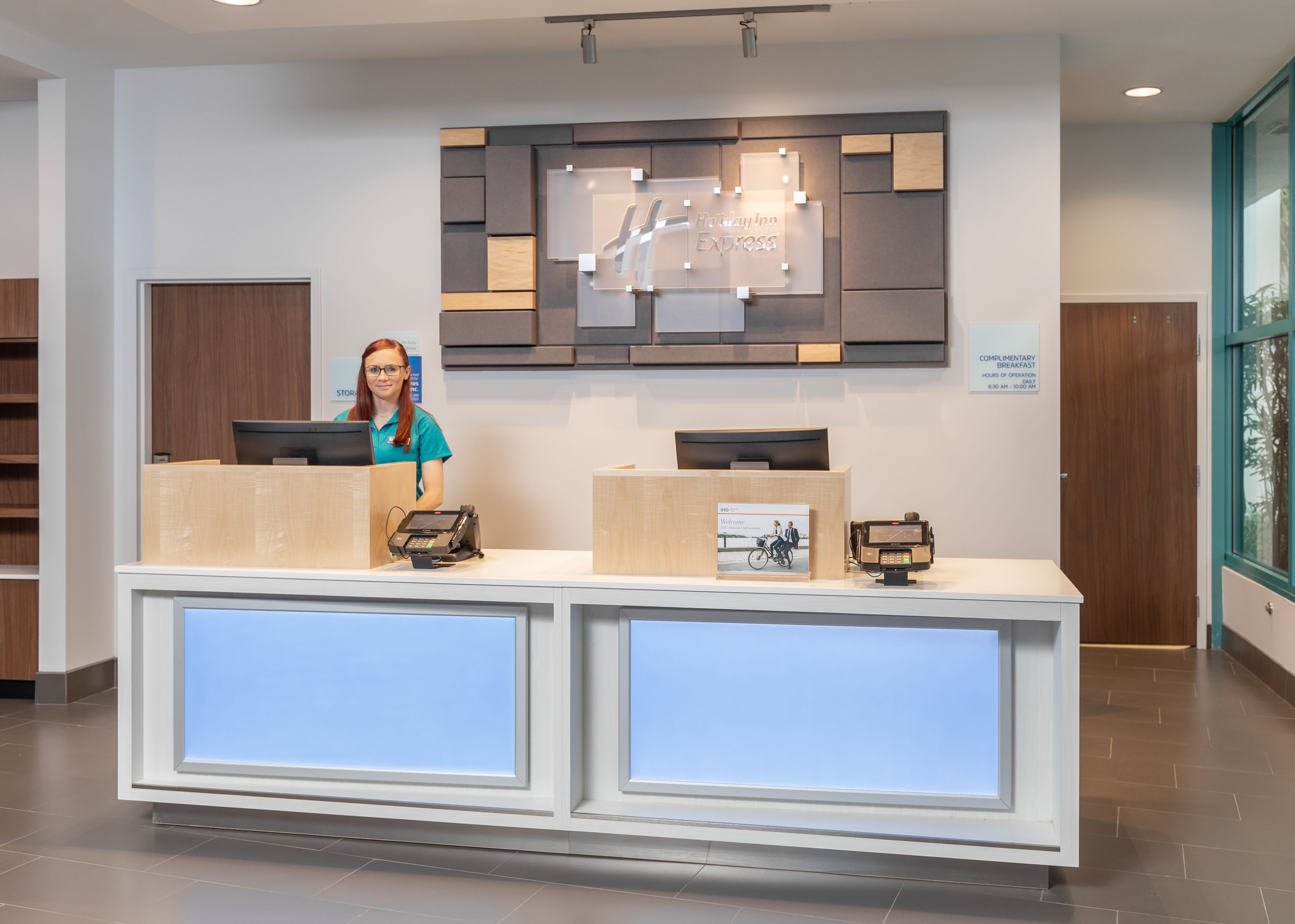 A hotel reception desk with a digital display, a complimentary breakfast sign, and a photo of a couple on a bike.