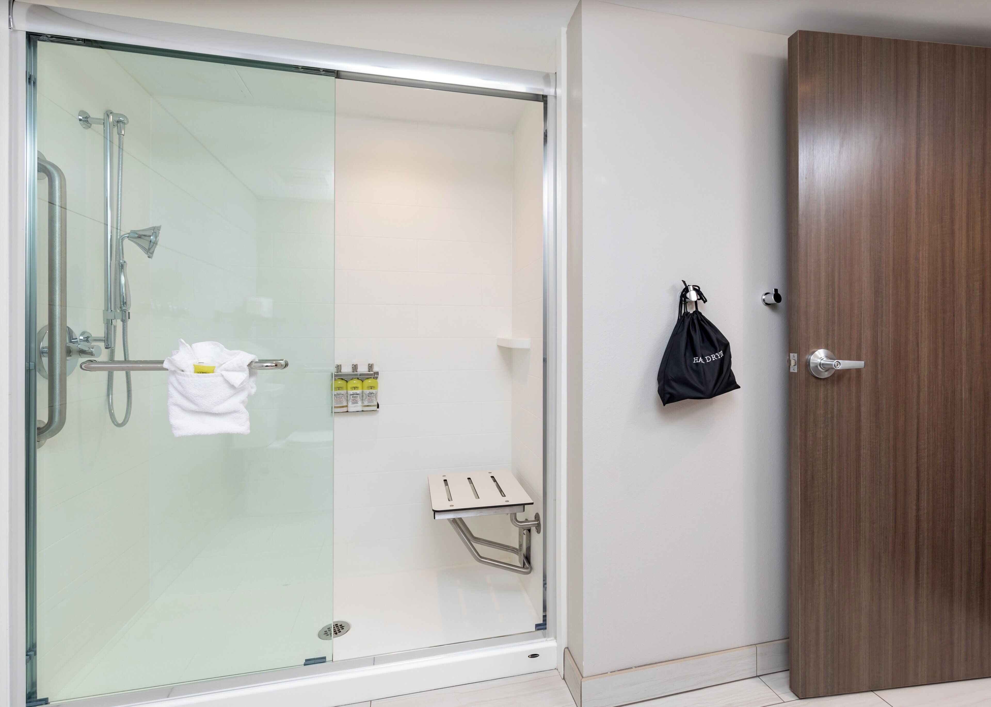 Ein modernes Badezimmer mit einer gläsernen Duschkabine, einem Handtuchhalter und einer Holztür.