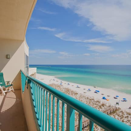 A balcony with a view of a beach, lounge chairs, and a wooden deck.