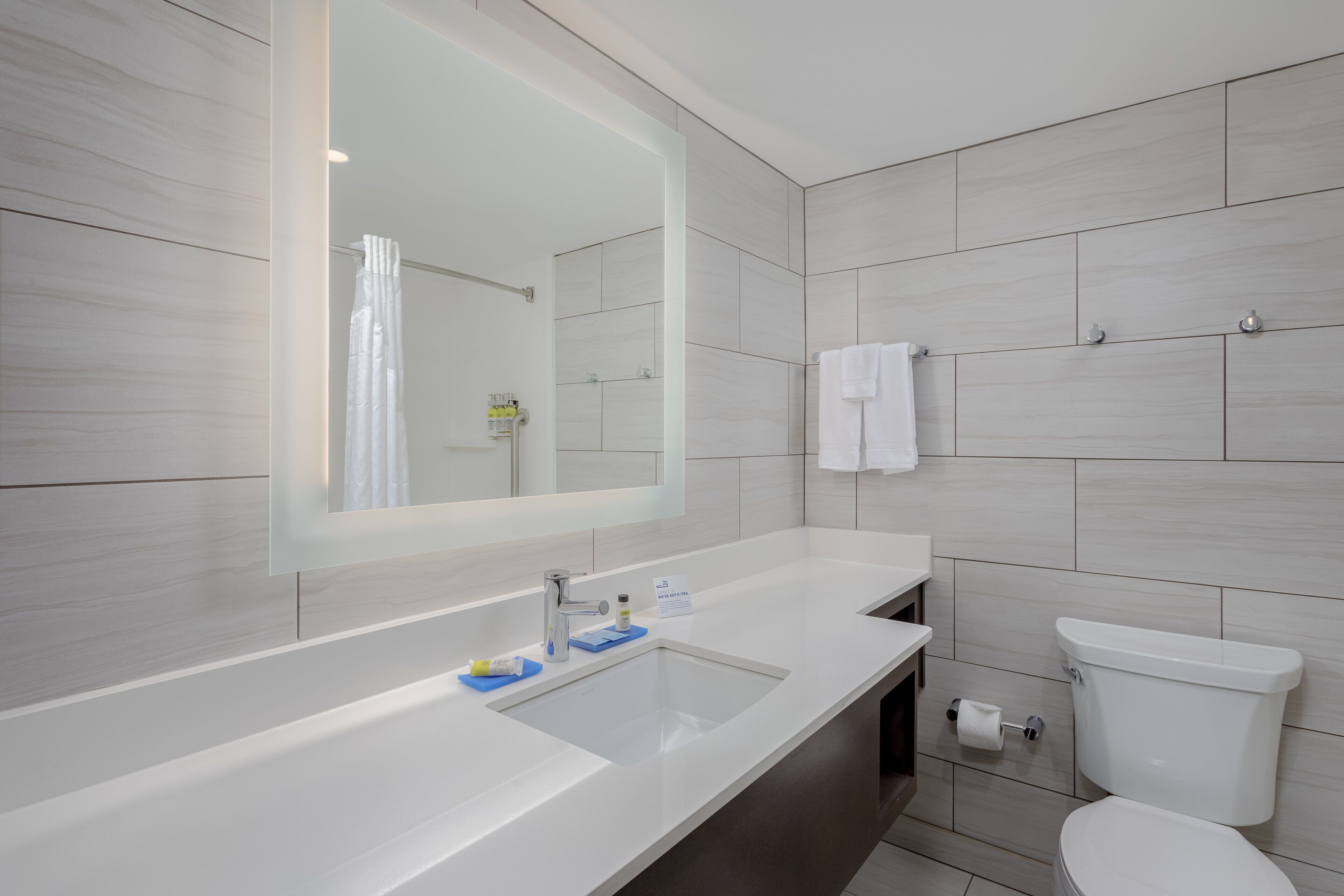 A modern bathroom with a large mirror, a sink, and a toilet.