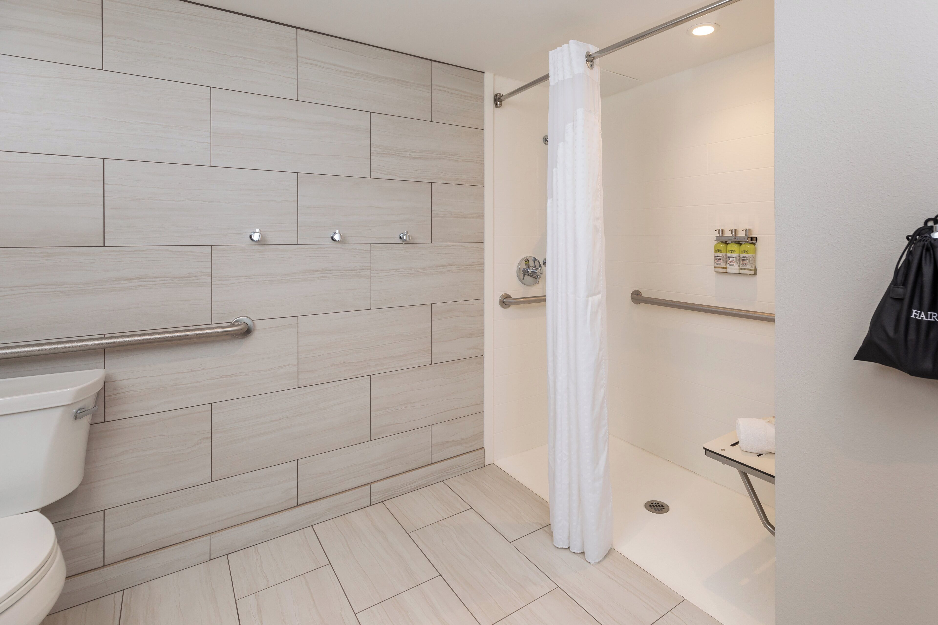 A modern bathroom with a shower, toilet, and handrails.