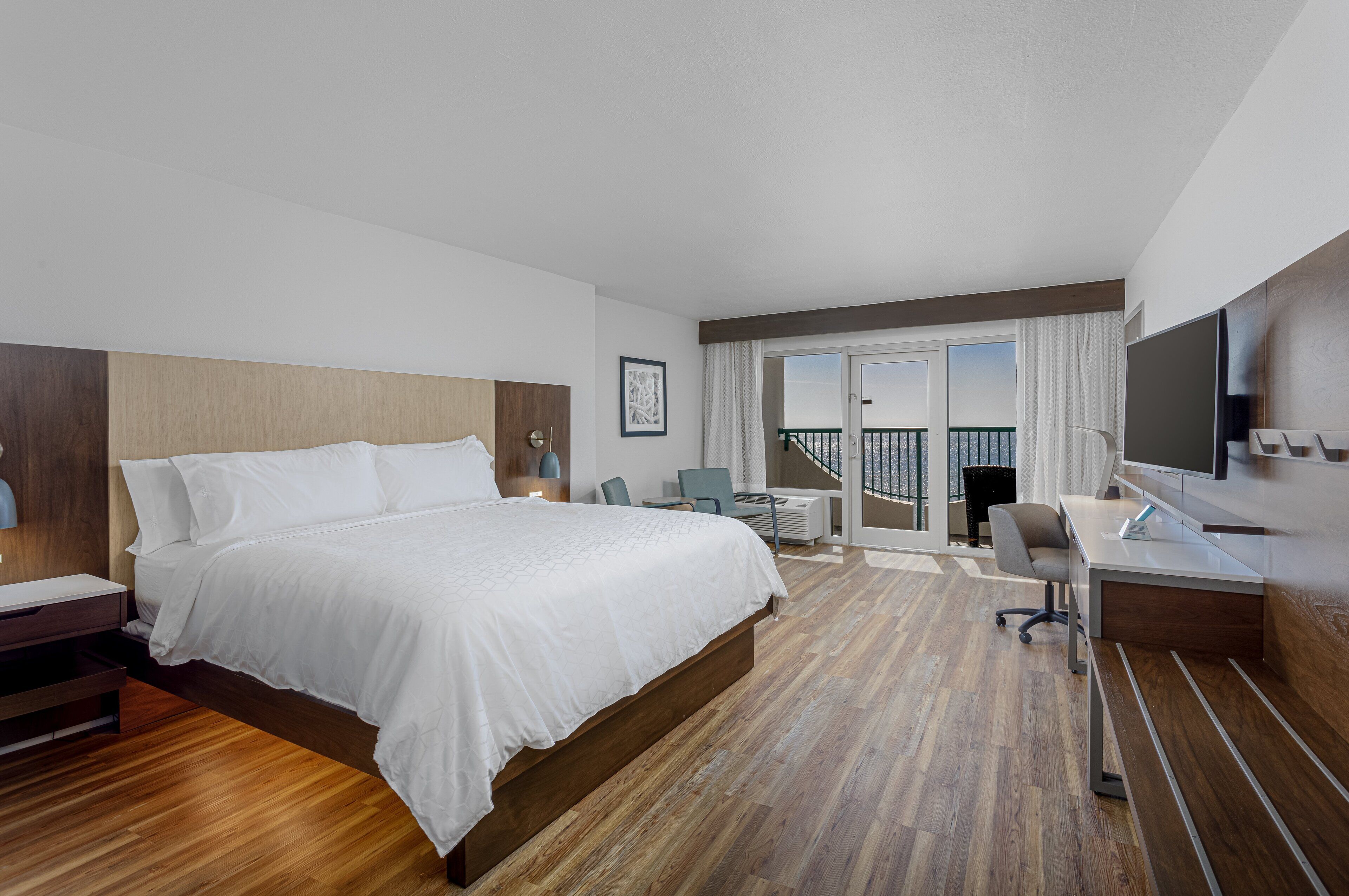 Ein Hotelzimmer mit einem großen Bett, einem Schreibtisch, einem Sessel, einem Fernseher und einem Balkon mit Blick.