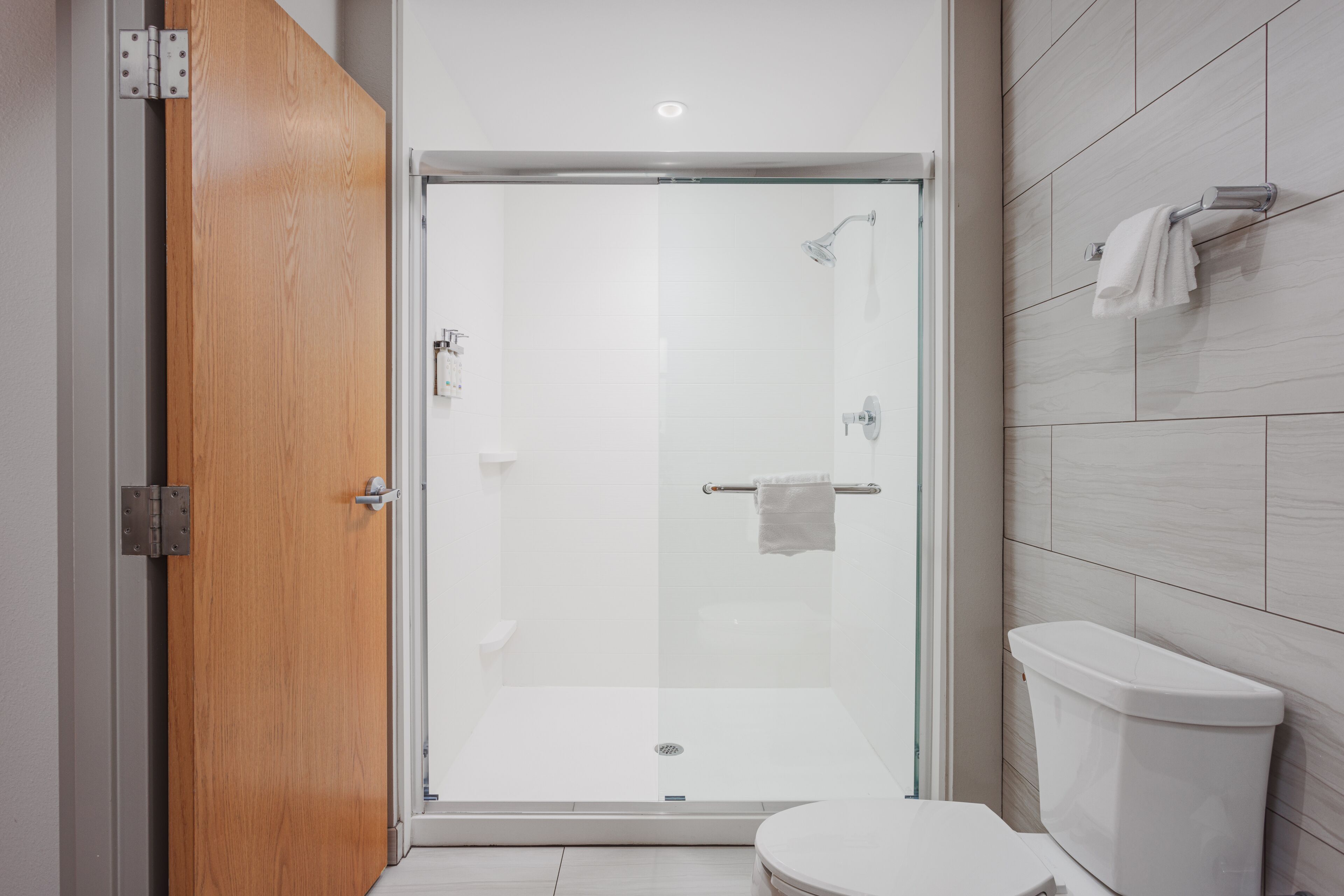 A modern bathroom with a glass-enclosed shower, a white toilet, and a wooden door.