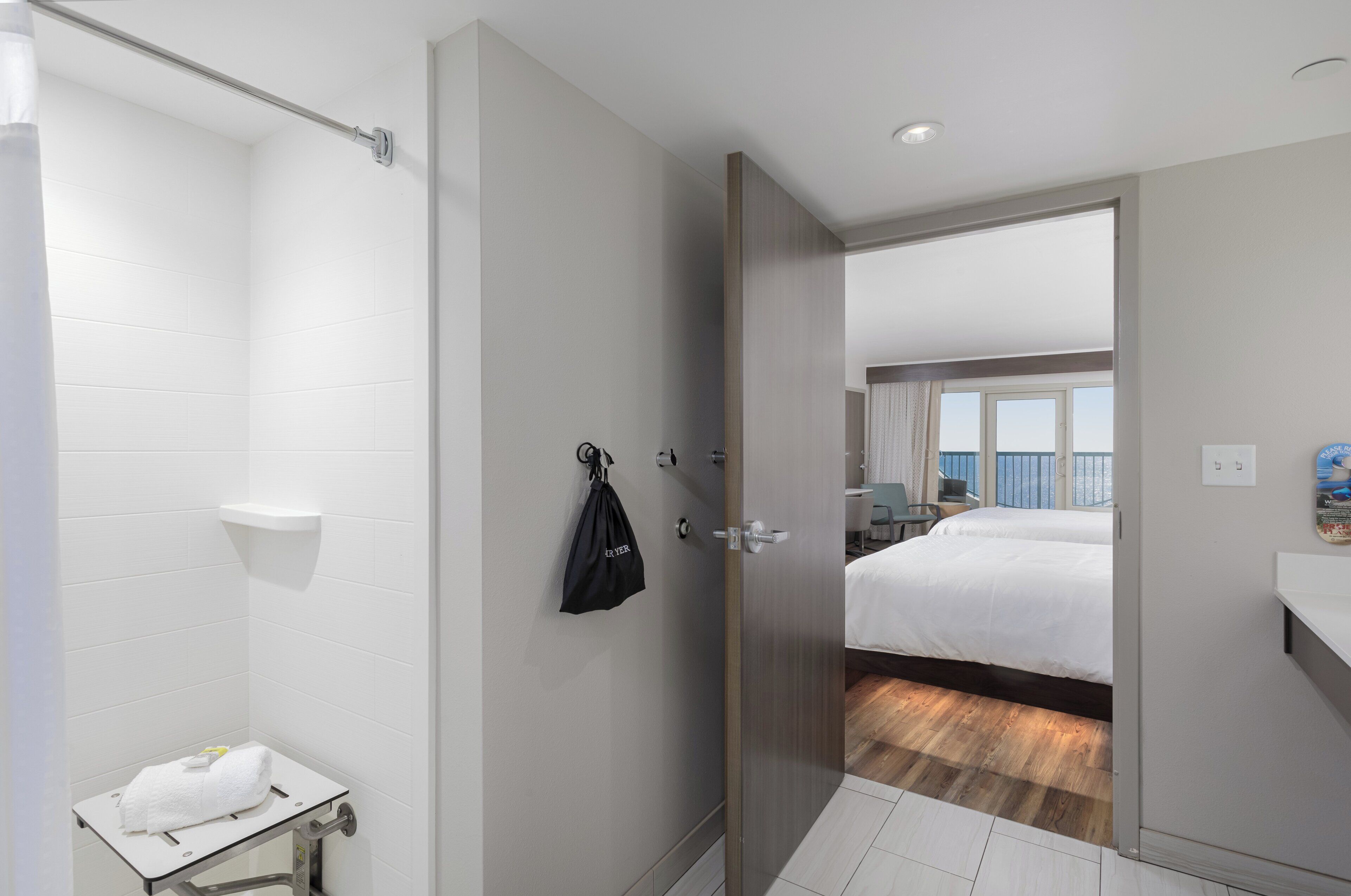 Une chambre d’hôtel avec une douche, une petite table avec une serviette, une porte donnant sur un balcon équipé d’un lit et offrant une vue.