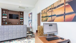 Un espacio de oficina moderno con un escritorio de madera, computadora y silla. Hay un televisor de pantalla plana grande en la pared y una estantería con varios objetos.