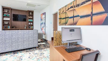 A modern office space with a wooden desk, computer, and chair. There is a large flat-screen TV on the wall and a bookshelf with various items.