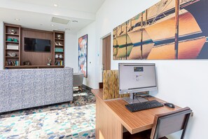 Un espacio de oficina moderno con un escritorio de madera, computadora y silla. Hay un televisor de pantalla plana grande en la pared y una estantería con varios objetos.