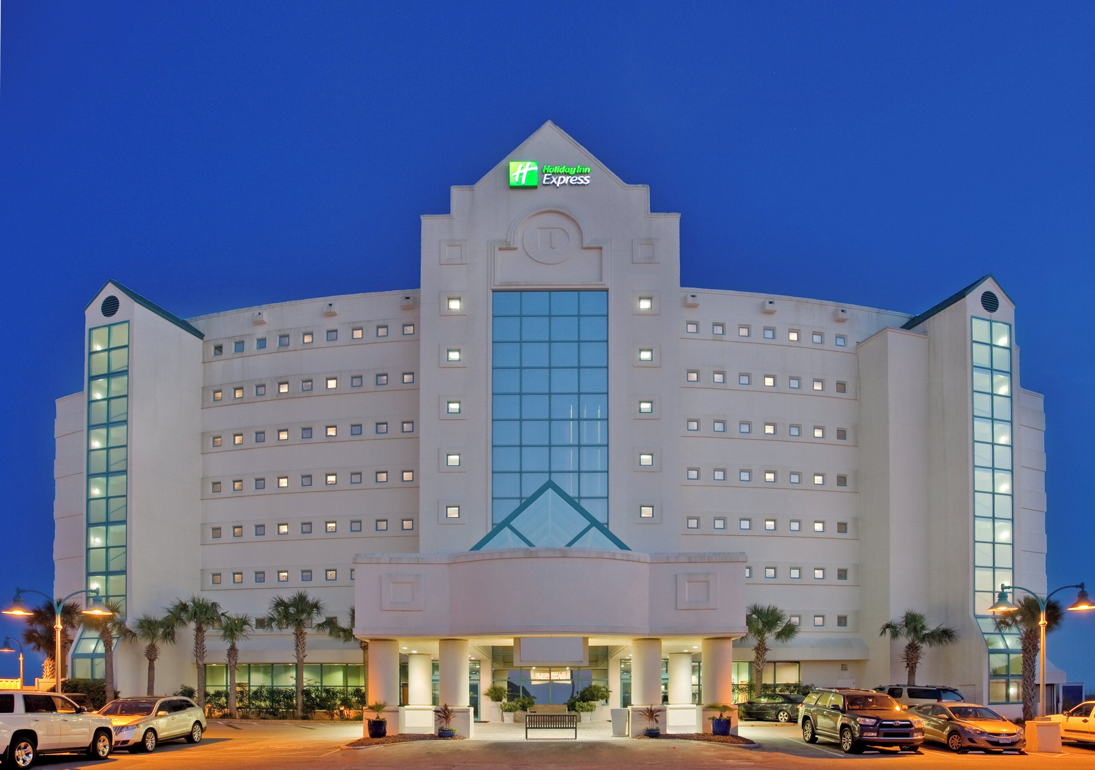 Et flere etagers Holiday Inn Express hotel med en markant indgang, palmer og en parkeringsplads.