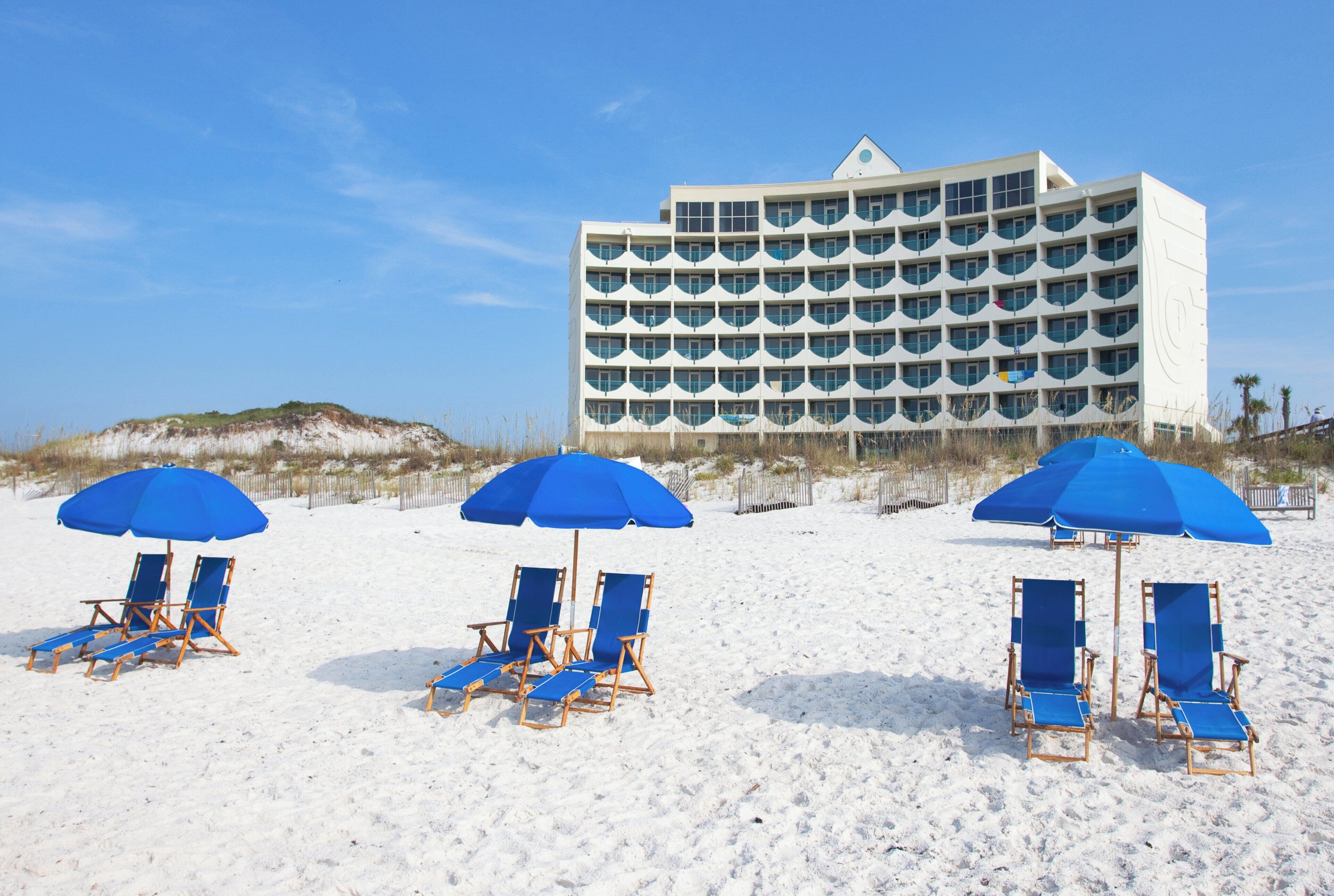 A beachfront hotel with multiple balconies, beach chairs, and umbrellas.