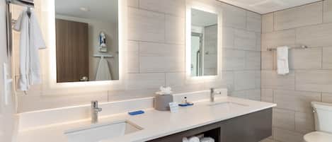 A modern bathroom with a large mirror, two sinks, a toilet, and a towel rack.