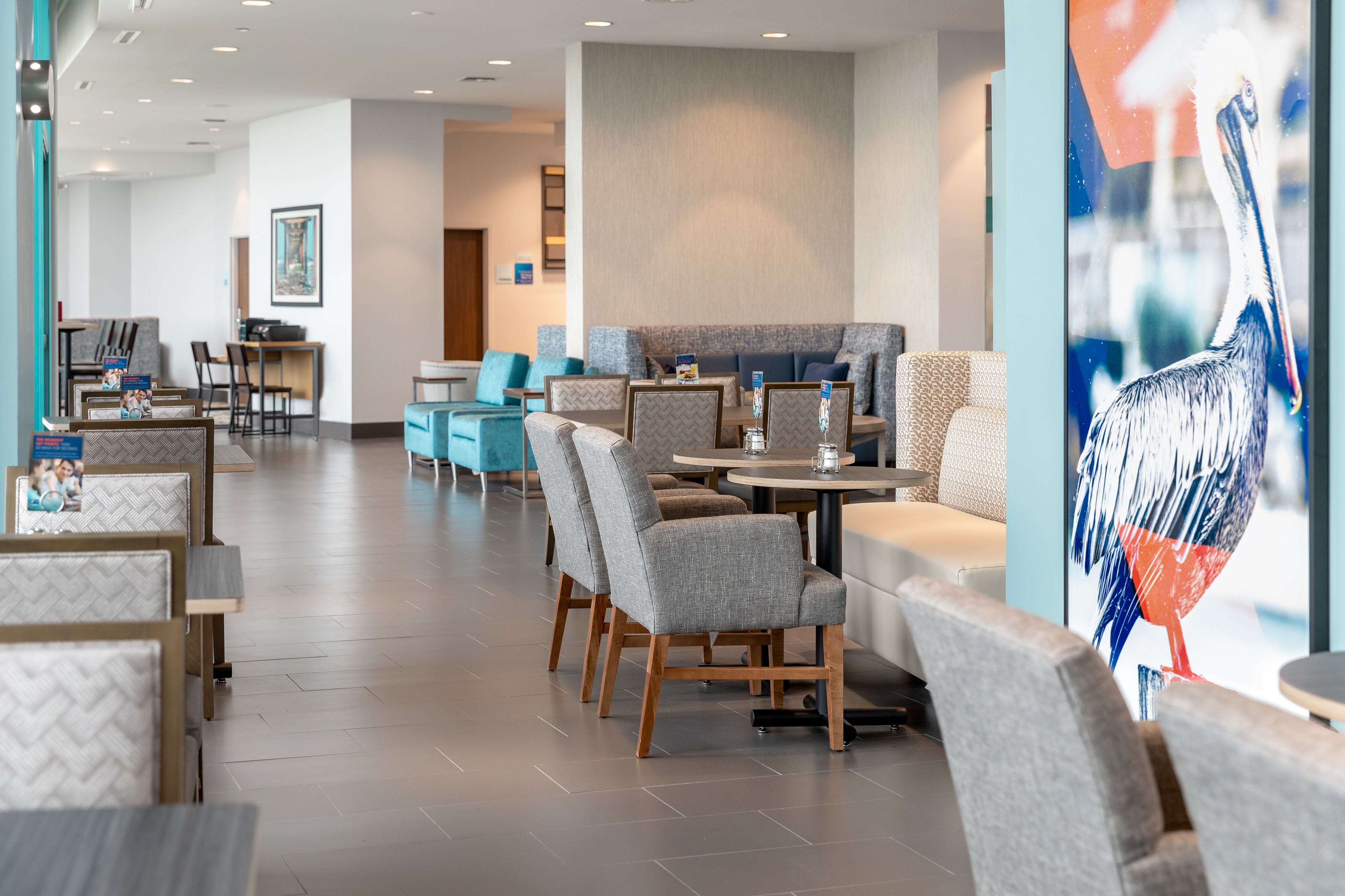 A modern hotel lobby with seating areas, a reception desk, and a large bird mural.
