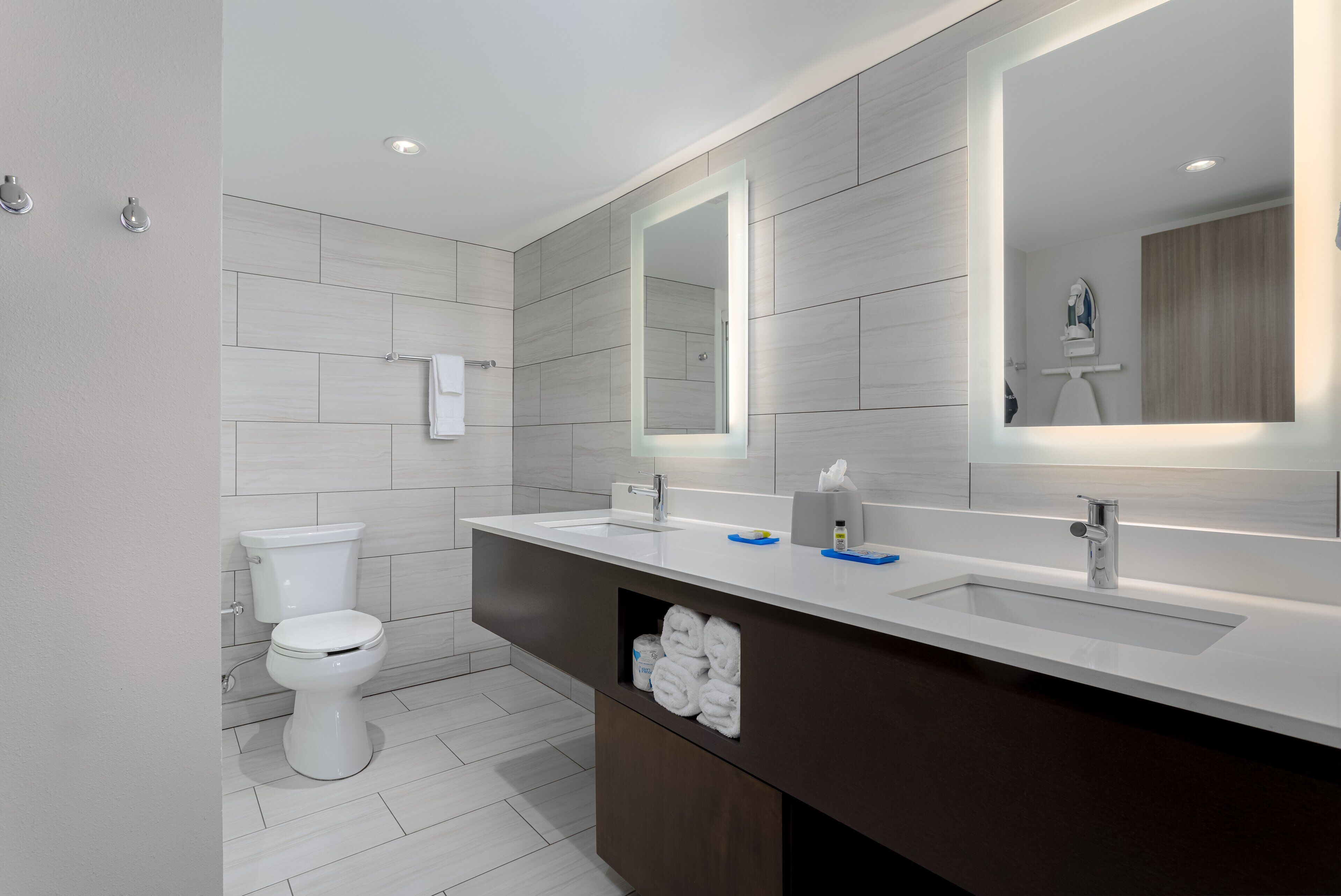 A modern bathroom with a white toilet, a large mirror, and a vanity with a sink.