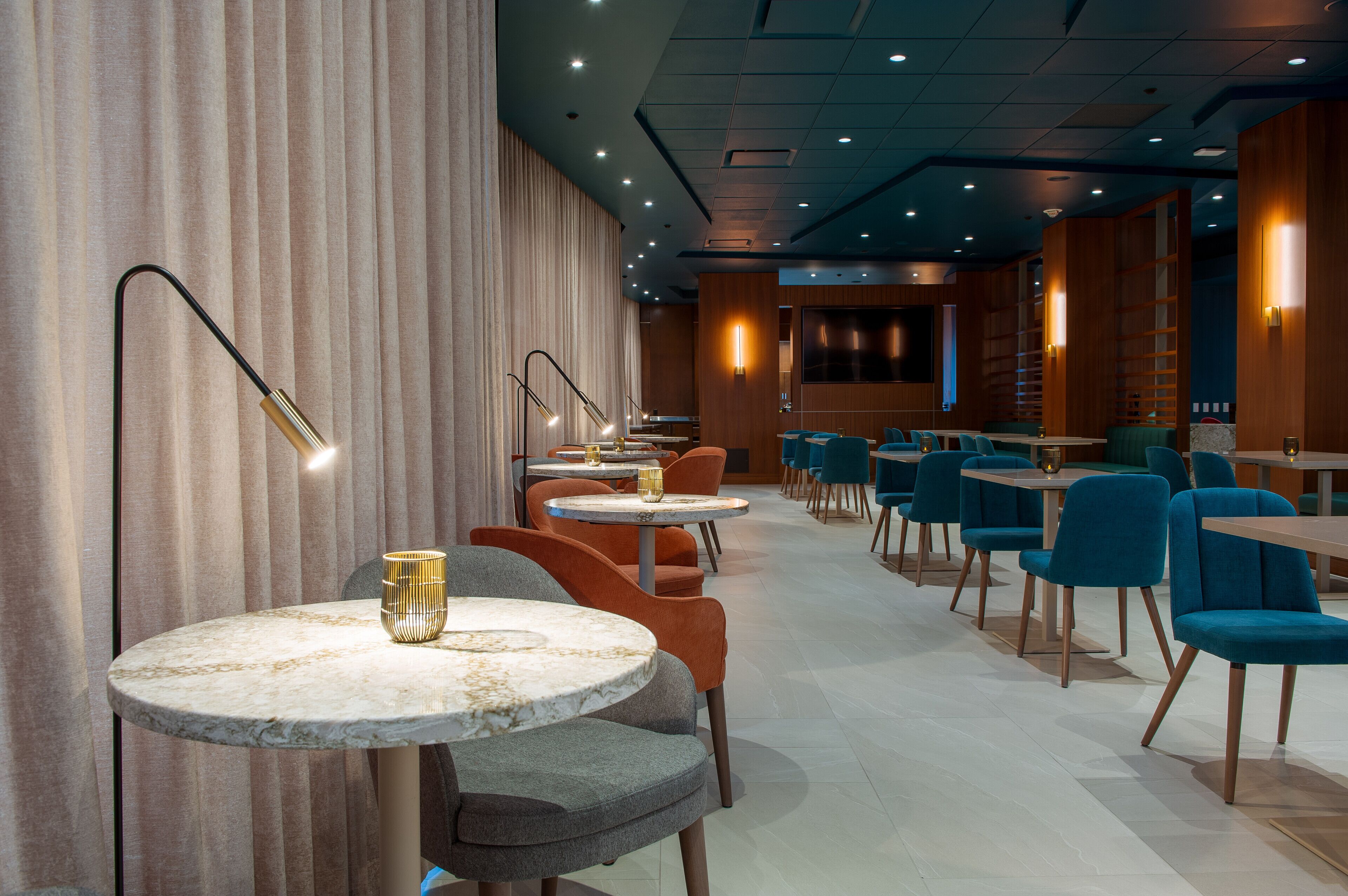 A modern restaurant with round marble tables, orange and blue chairs, and warm lighting.
