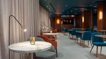 A modern restaurant with round marble tables, orange and blue chairs, and warm lighting.
