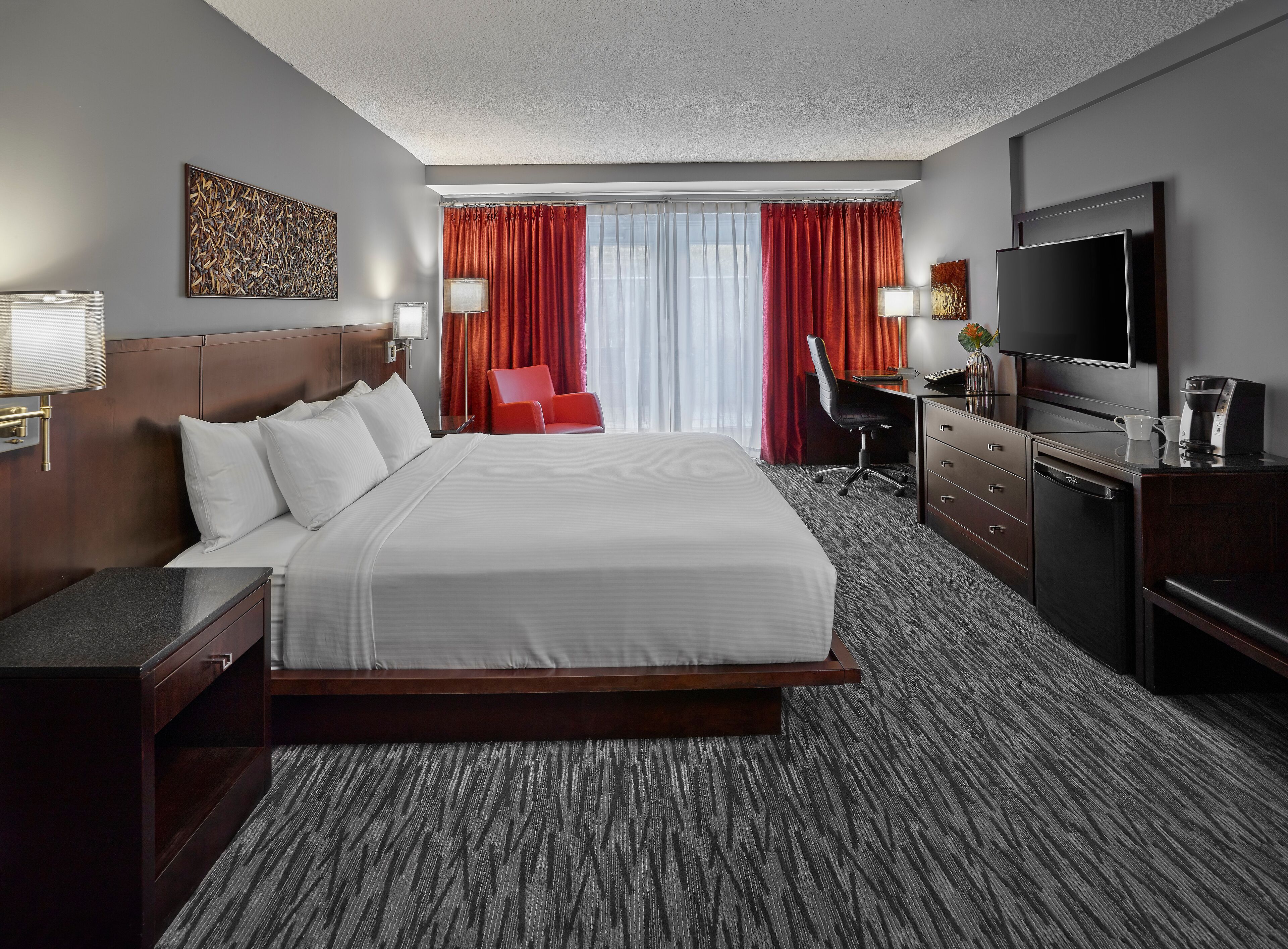 Habitación de hotel con una cama grande, un escritorio con silla, televisor y cafetera.