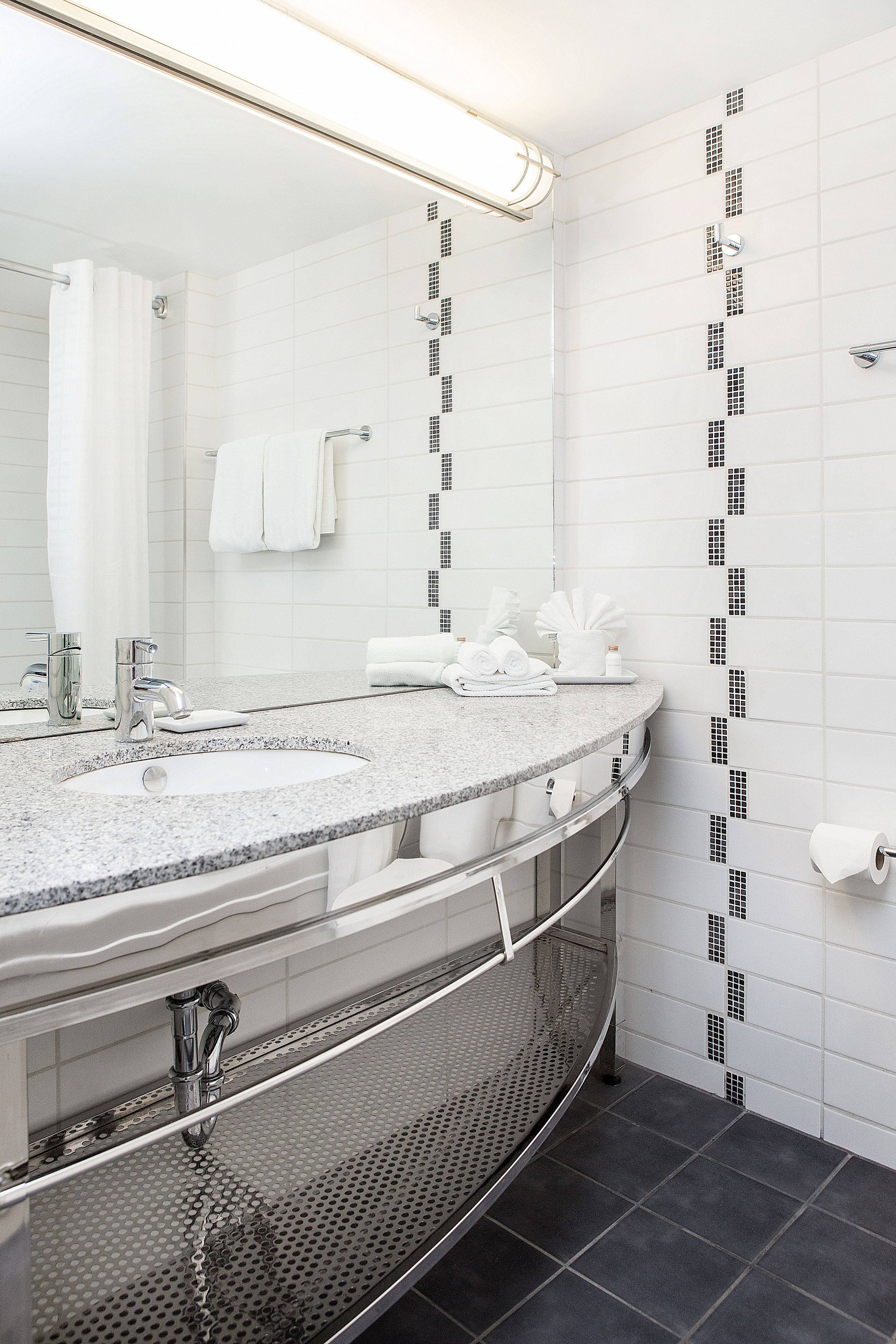 A modern bathroom with a granite countertop, a large mirror, a shower area, and a toilet paper holder.