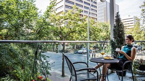 A balcony with a table and chairs, overlooking a street with cars and buildings.