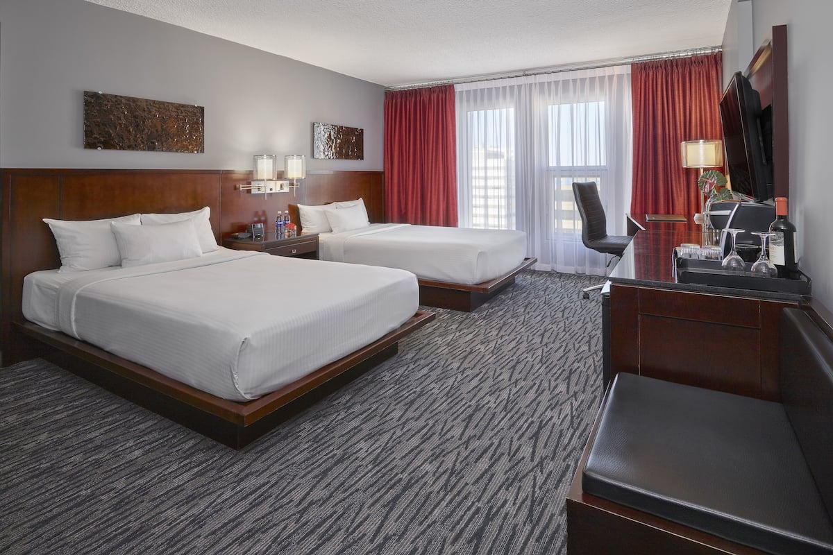 A hotel room with two beds, a desk, a chair, and a TV.