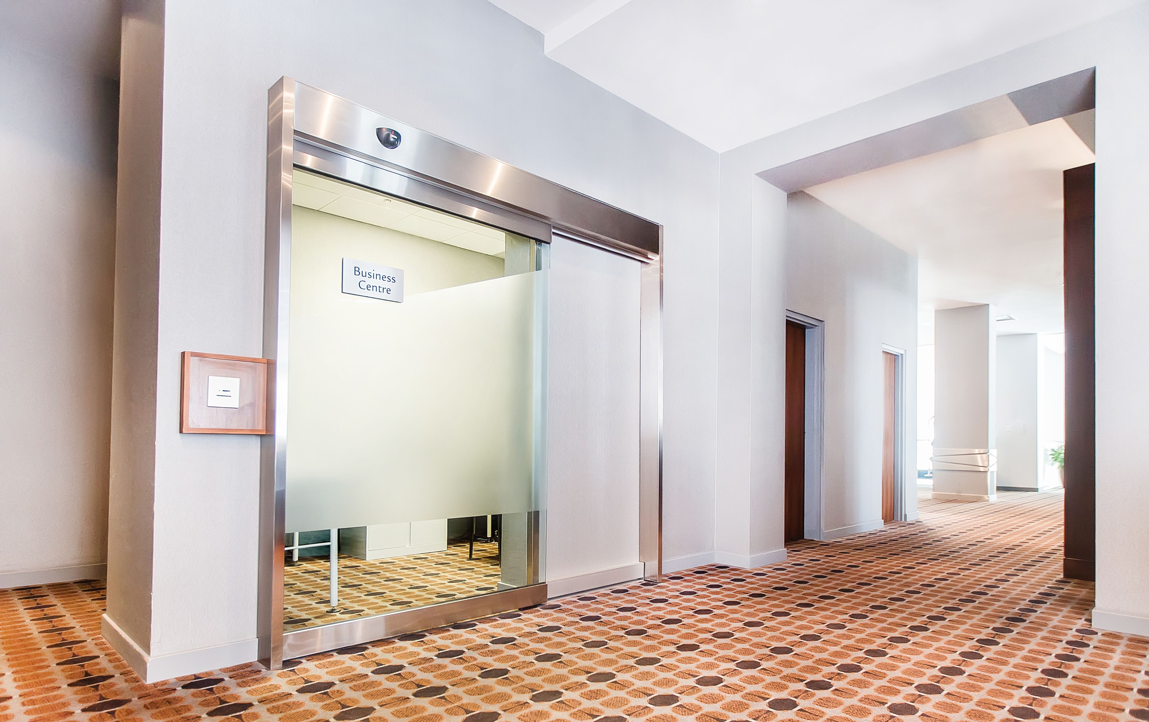 A modern elevator with a business center sign, a patterned carpet, and a hallway with doors.
