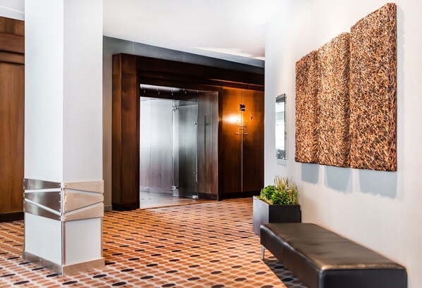 A modern lobby with a patterned carpet, a reception desk, a seating area, and a wall-mounted artwork.
