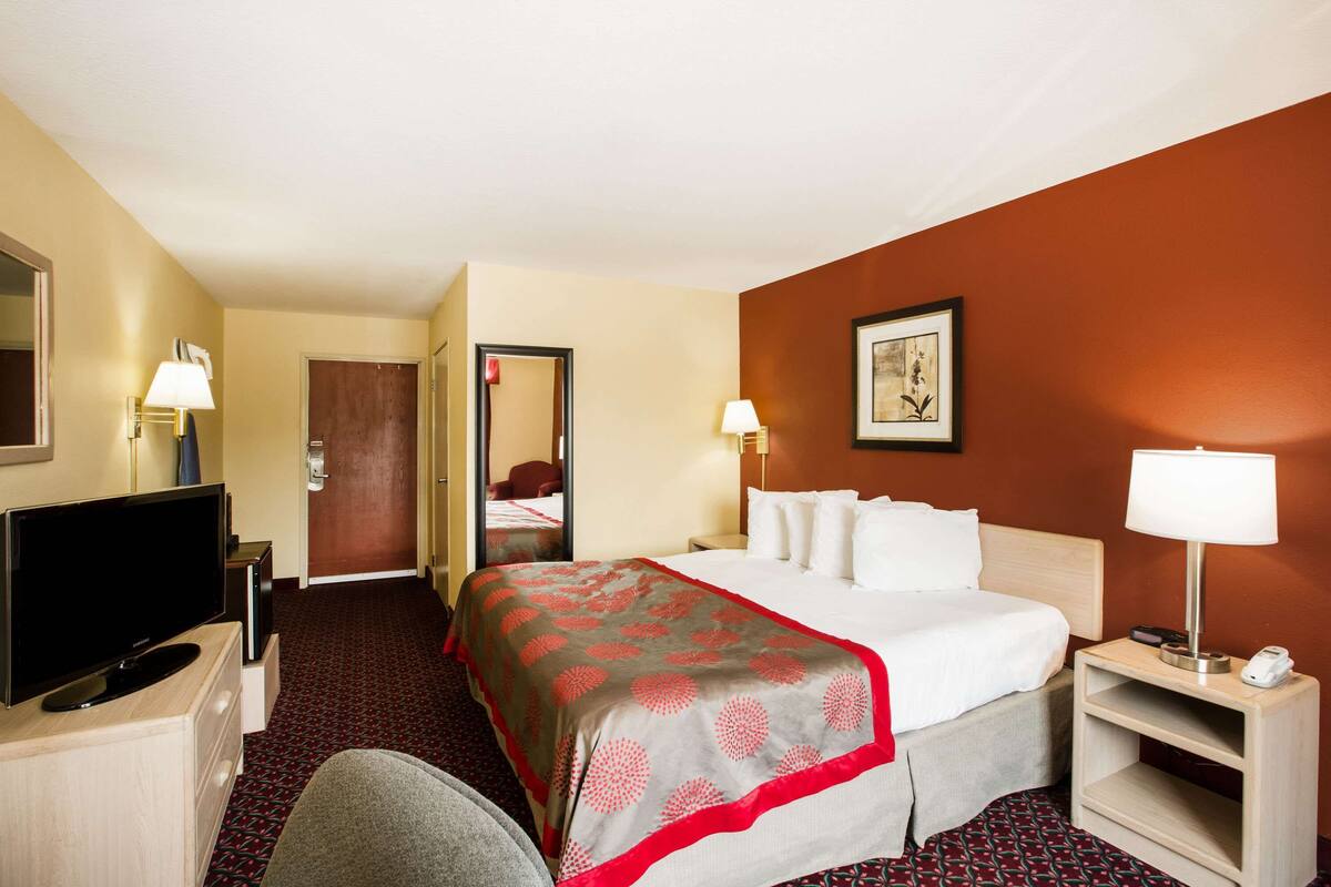 A hotel room with a bed, a TV, a desk, and a chair.