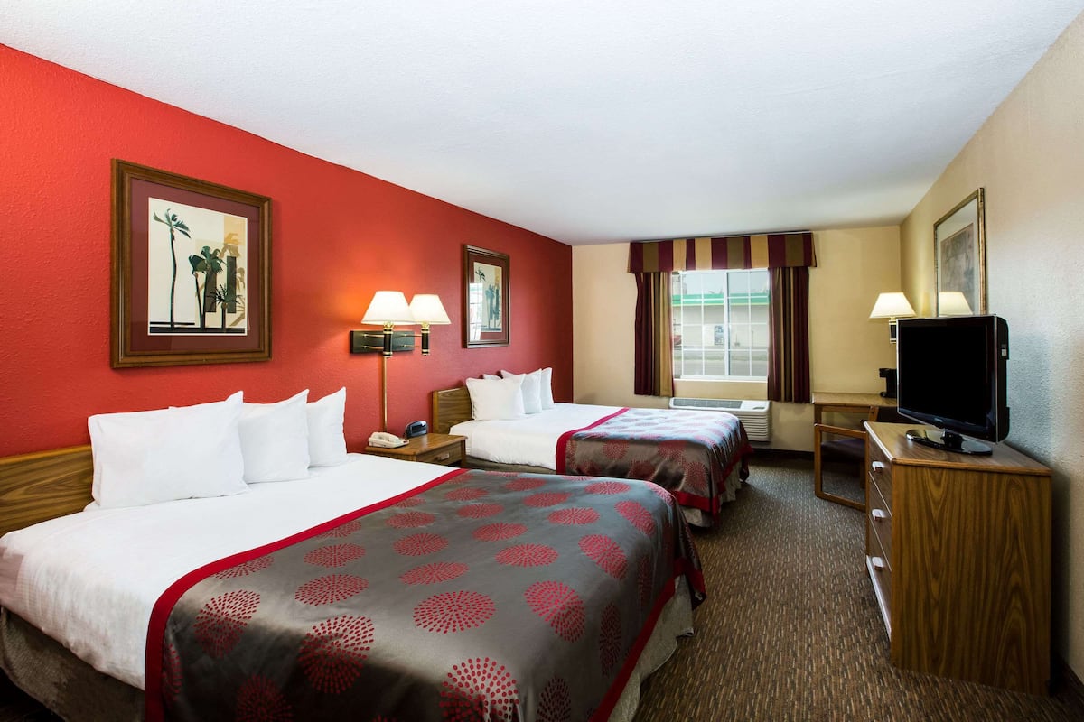A hotel room with two beds, a television, a desk, and a window with curtains.