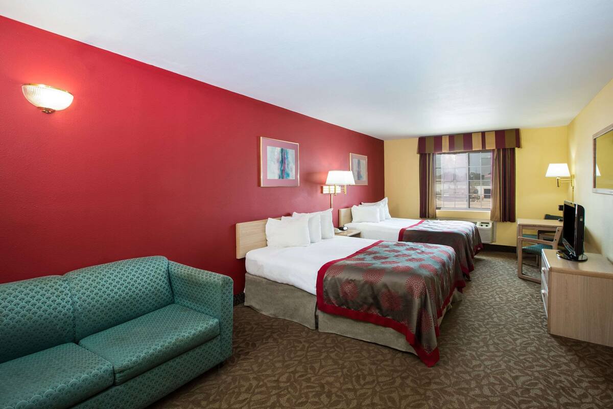 A hotel room with two beds, a sofa, a desk, and a TV.