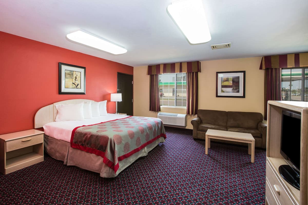 A hotel room with a bed, a sofa, a TV, and a window with curtains.