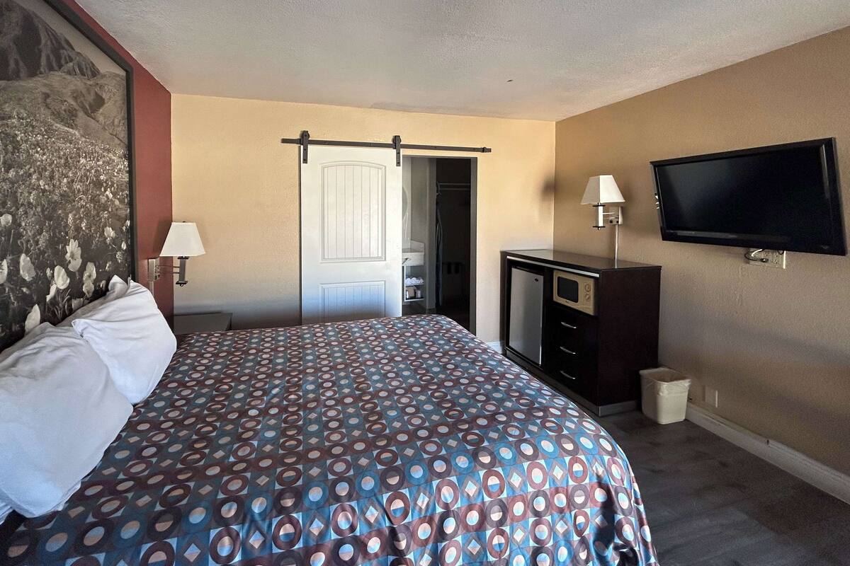 A hotel room with a bed, a desk, a TV, and a door leading to a bathroom.