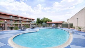 A swimming pool with lounge chairs and umbrellas, surrounded by buildings with a red-tiled roof.