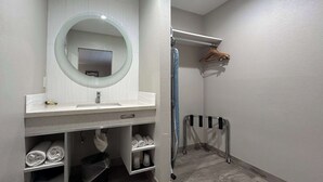 A bathroom with a white vanity, a round mirror, a towel rack, and a shower area.