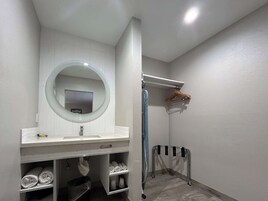 Un baño con tocador blanco, espejo redondo, toallero y zona de ducha.