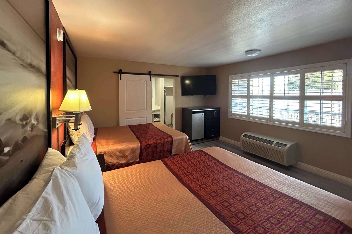 A hotel room with two beds, a TV, a heater, and a window with blinds.