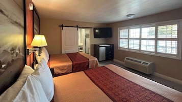 A hotel room with two beds, a TV, a heater, and a window with blinds.