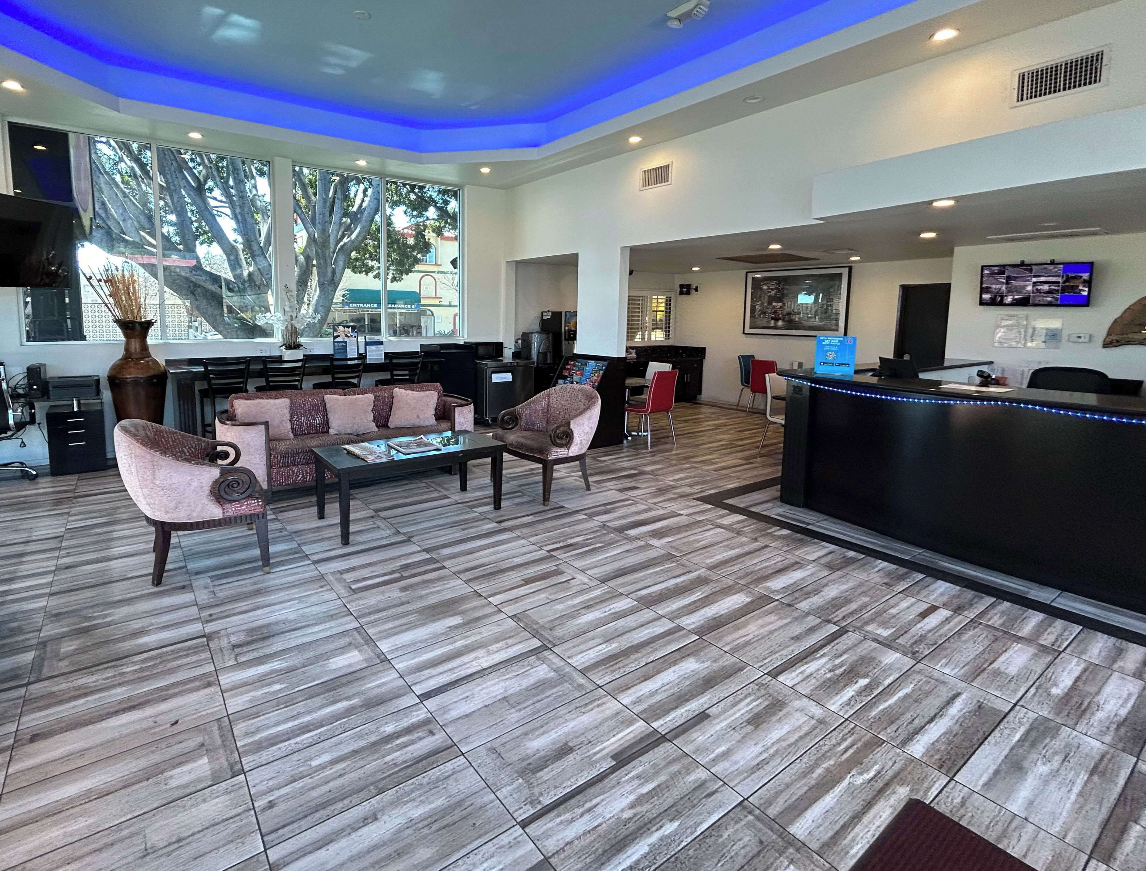Un espace d’accueil moderne comprenant un comptoir de réception, un coin salon et de grandes fenêtres donnant sur des arbres et un bâtiment à l’extérieur.
