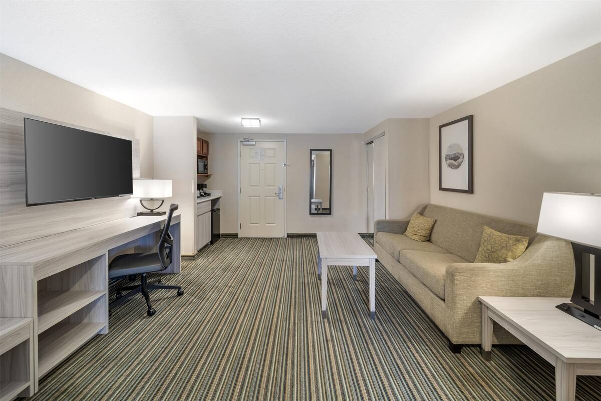 A hotel room with a flat-screen TV, a desk, a sofa, and a coffee table.