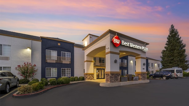 A Best Western Plus hotel with a modern facade, multiple windows, and a parking area with cars and a van. - Best Western Plus Twin View Inn & Suites (Redding)