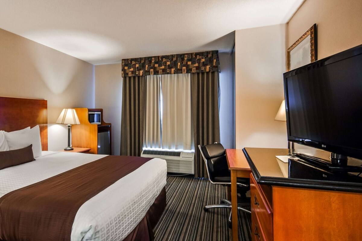 A hotel room with a bed, desk, television, and curtains.