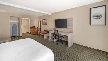 Een hotelkamer met een groot bed, een bureau met stoel, een televisie en een ingelijst schilderij aan de muur.